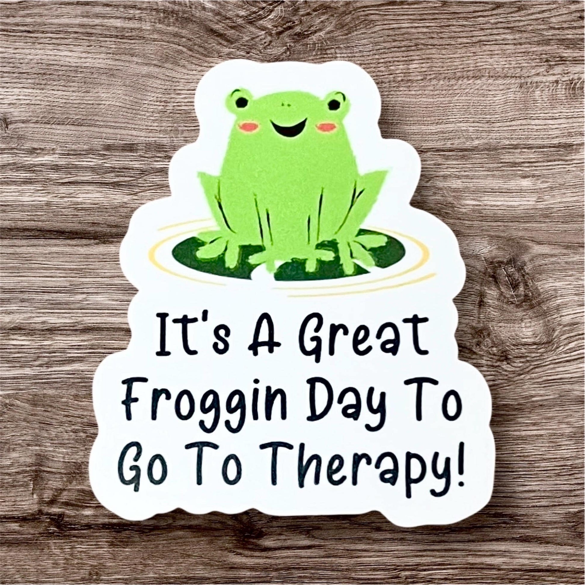 A colorful vinyl sticker featuring a smiling green frog sitting on a yellow circle with the phrase 'It's a GREAT FROGGIN DAY TO GO TO THERAPY!' in bold, cheerful lettering.